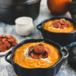 squash soup topped with sliced sausage and drizzled with cream served in black ceramic pumpkins