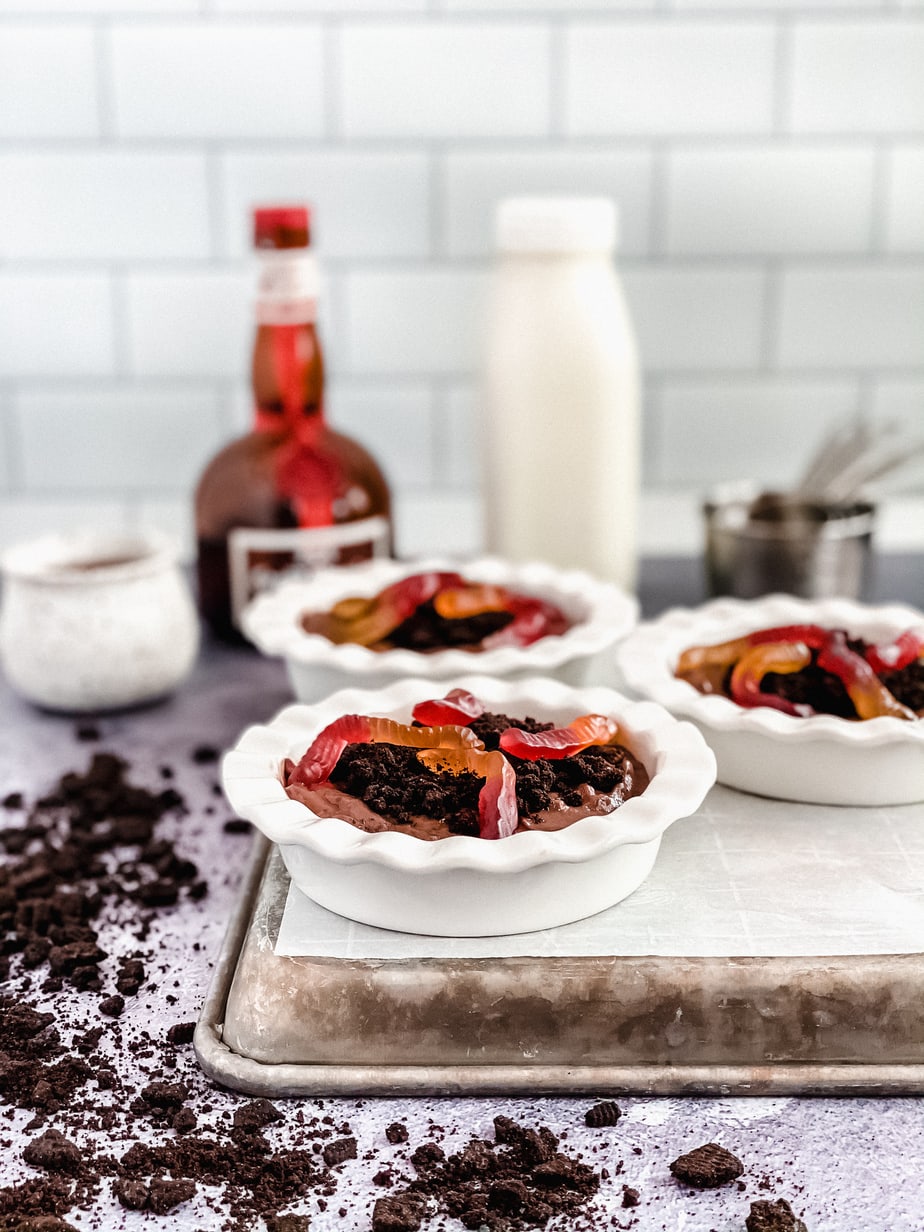 chocolate pudding in white round dishes topped with crushed Oreo cookies and gummy worms