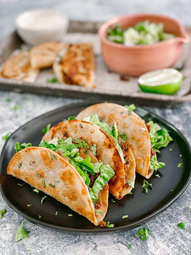 crispy beef and cheese tacos on a serving plate topped with lettuce