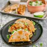 3 crispy tacos with sour cream and lettuce on a black plate