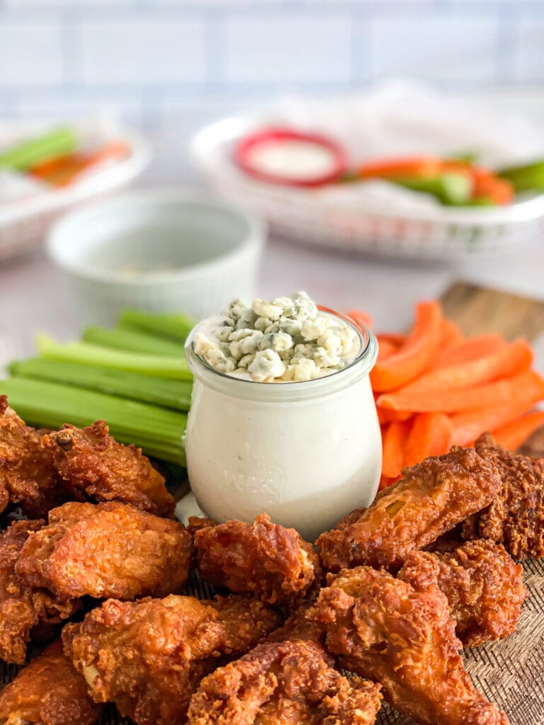 blue cheese dressing in a jar on a platter with chicken wings and celery and carrots