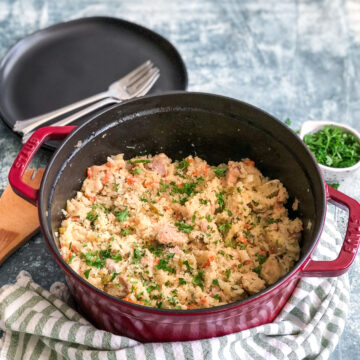 dutch oven with chicken and rice topped with parsley served next to a stack of serving plates and forks