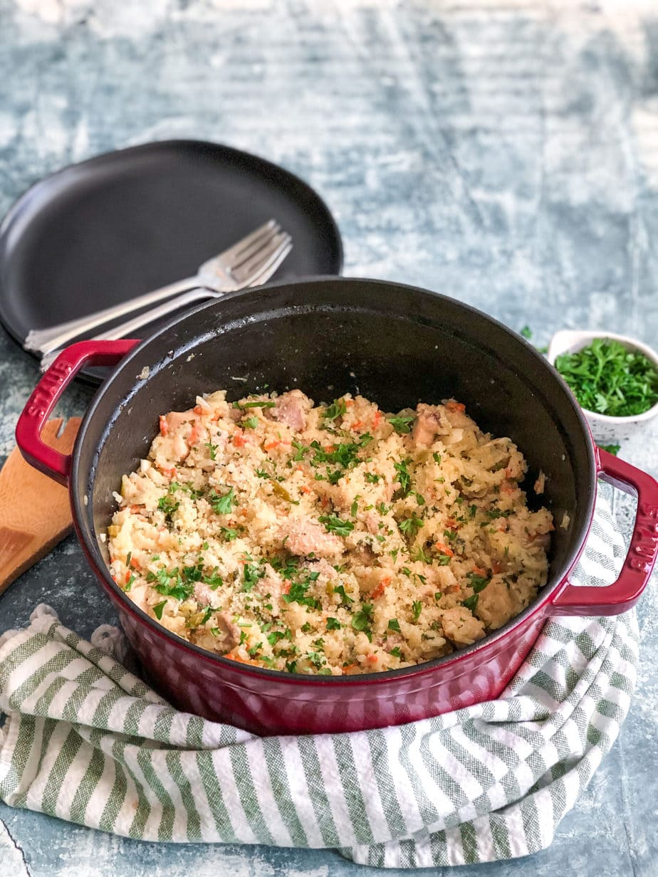 dutch oven with chicken and rice topped with parsley served next to a stack of serving plates and forks