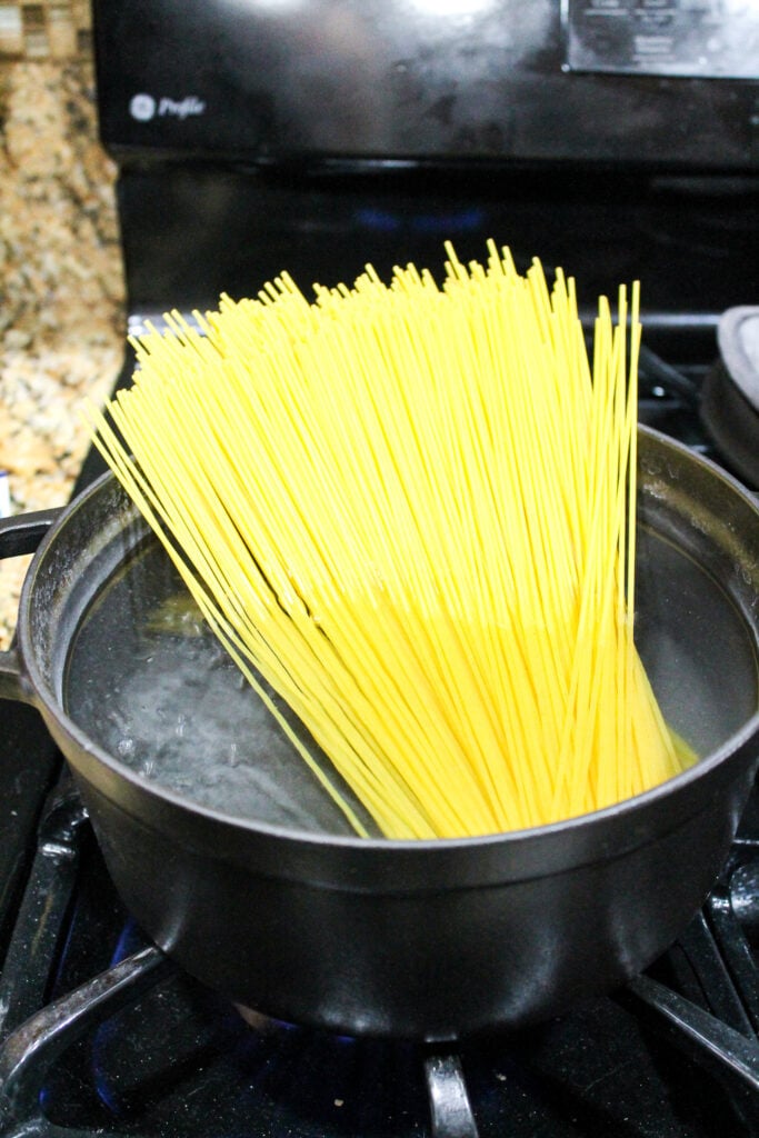 dry spaghetti being dropped into a pot of boiling water
