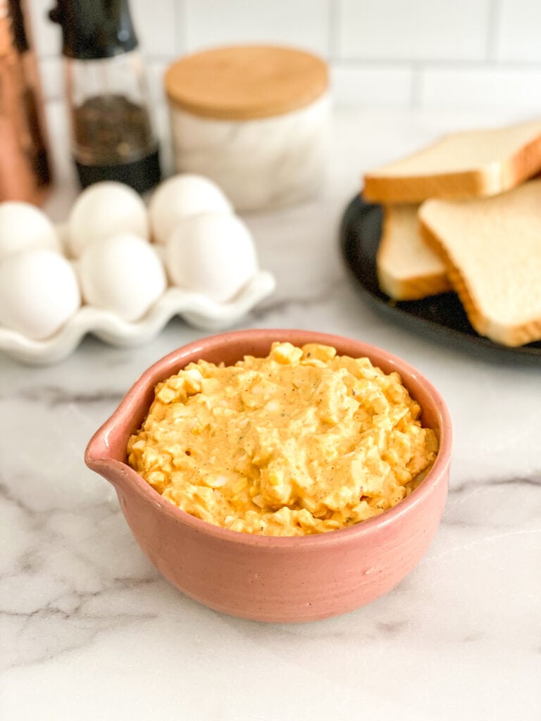 egg salad in a pink serving bowl with ingredients in the background
