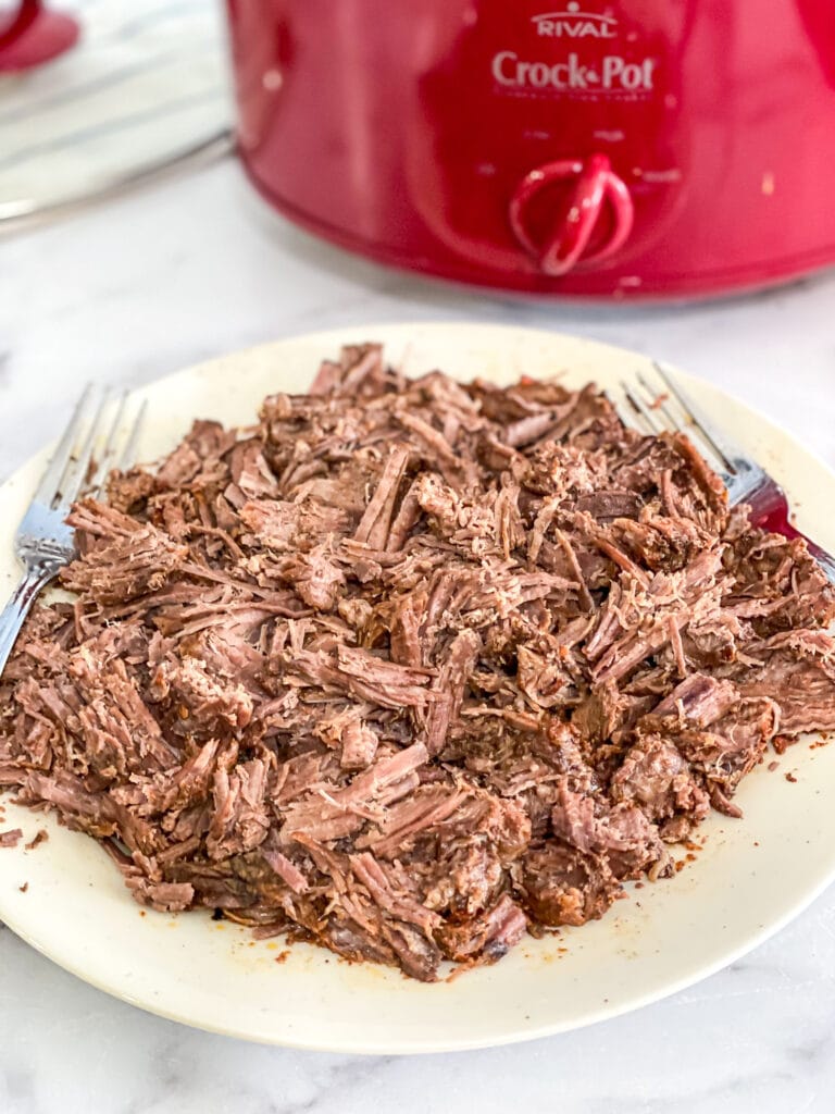 chipotle shredded beef shredded on a plate in front of the crock pot