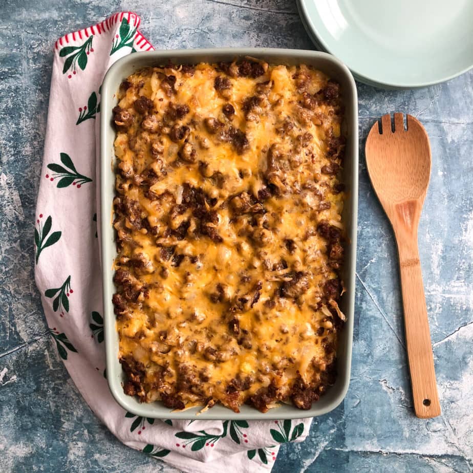 cheesy sausage and hash browns casserole after being baked in the oven, in a green casserole dish with serving spoon