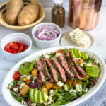 steak salad dressed on a serving platter with extra ingredients in the background