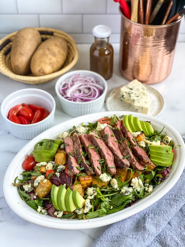 steak salad dressed on a serving platter with extra ingredients in the background