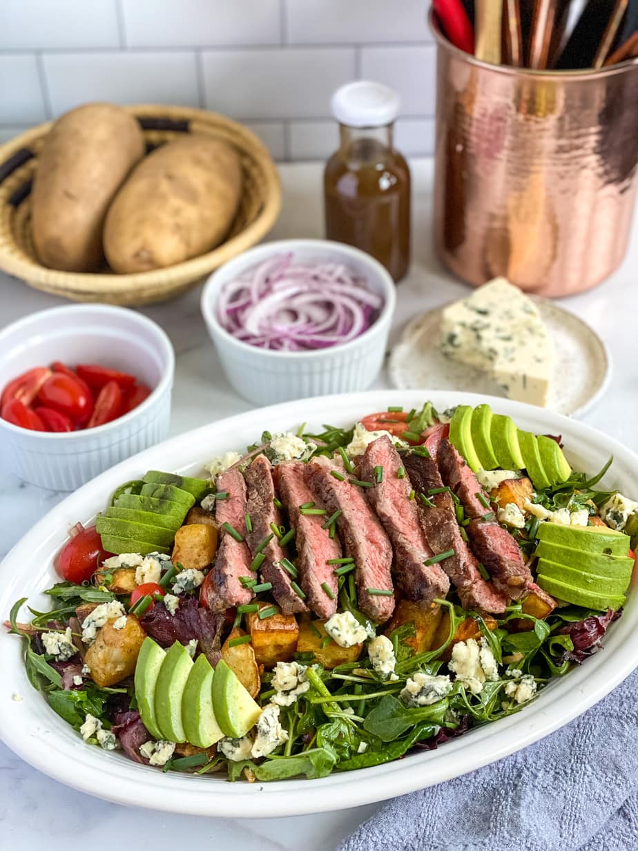 steak salad dressed on a serving platter with extra ingredients in the background