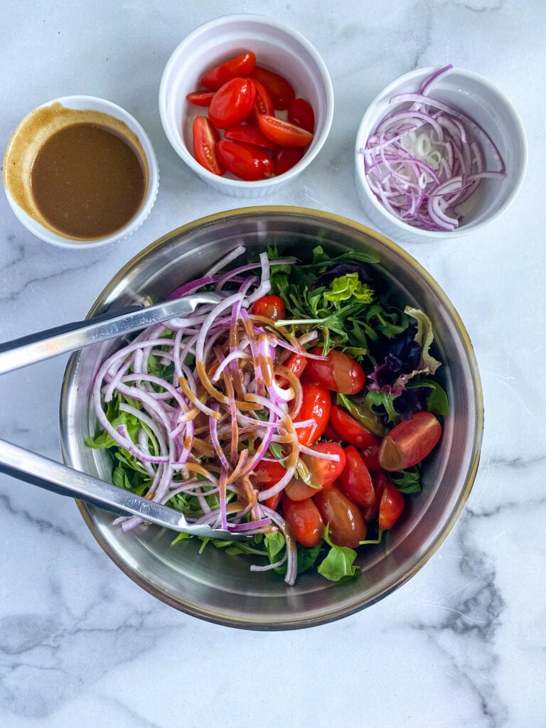 simple garden salad with mixed greens, red onion and tomatoes topped with dressing