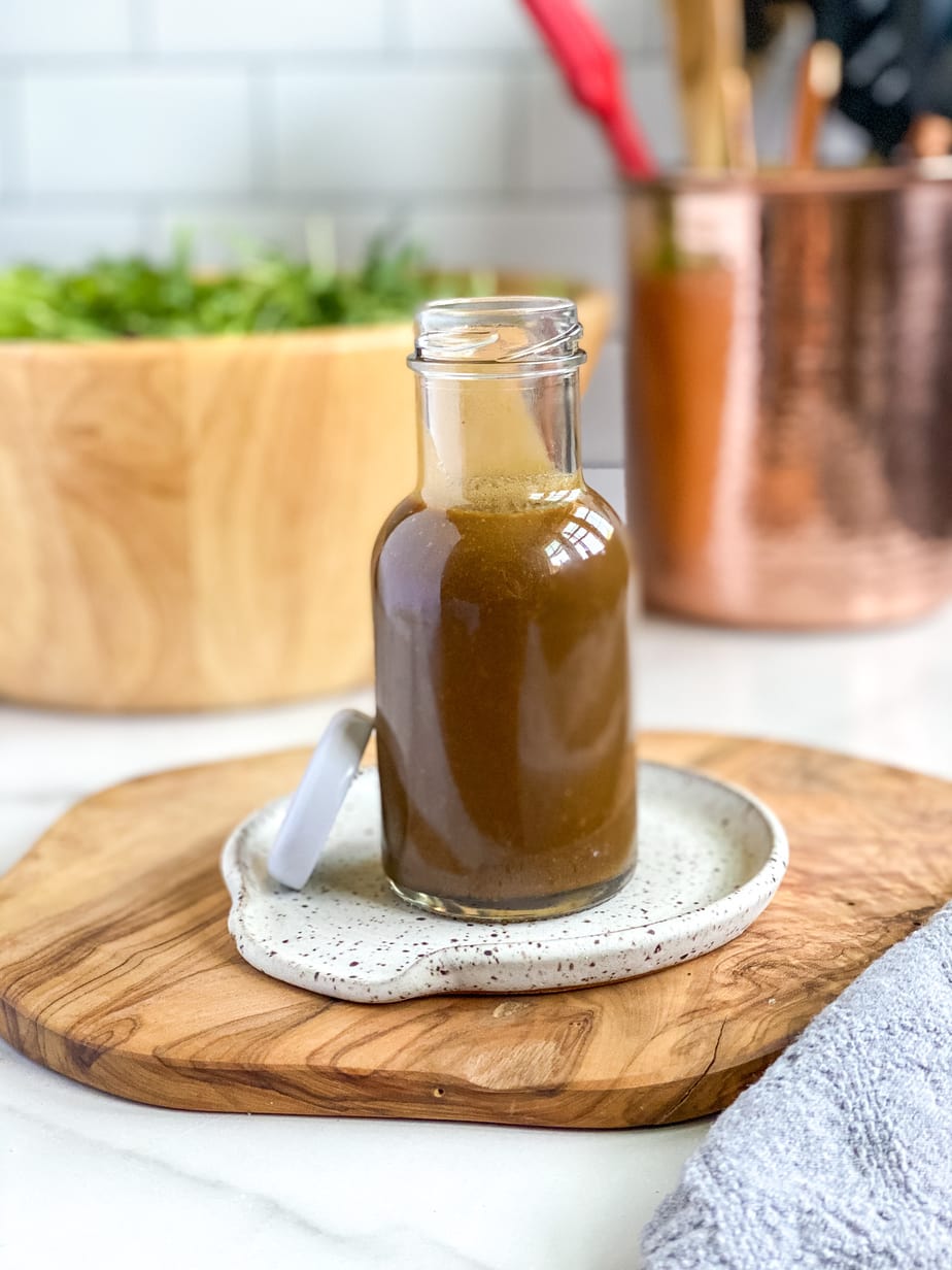 creamy balsamic dijon dressing in small glass jar for serving with bowl of salad in the background