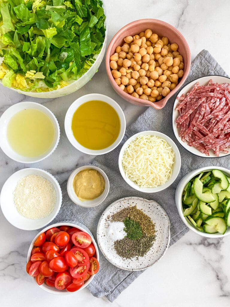 ingredient shot for the Italian chopped salad with all the ingredients measured and ready. In the shot you can find Romain, chickpeas, salami, cucumber, tomatoes, mozzarella cheese and all of the dressing ingredients.