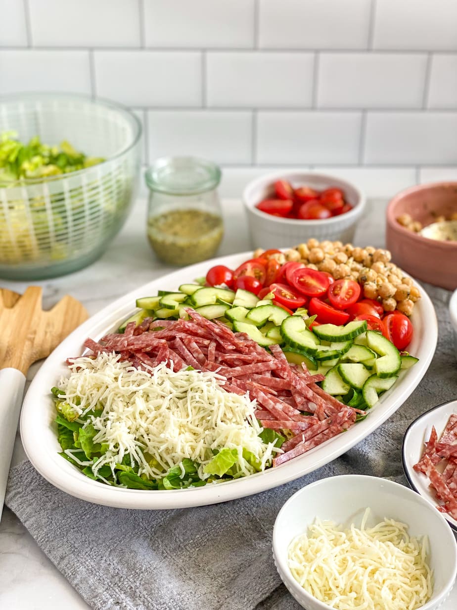 Italian chopped salad with ingredients unmixed on serving plate. Extra ingredients are in the background