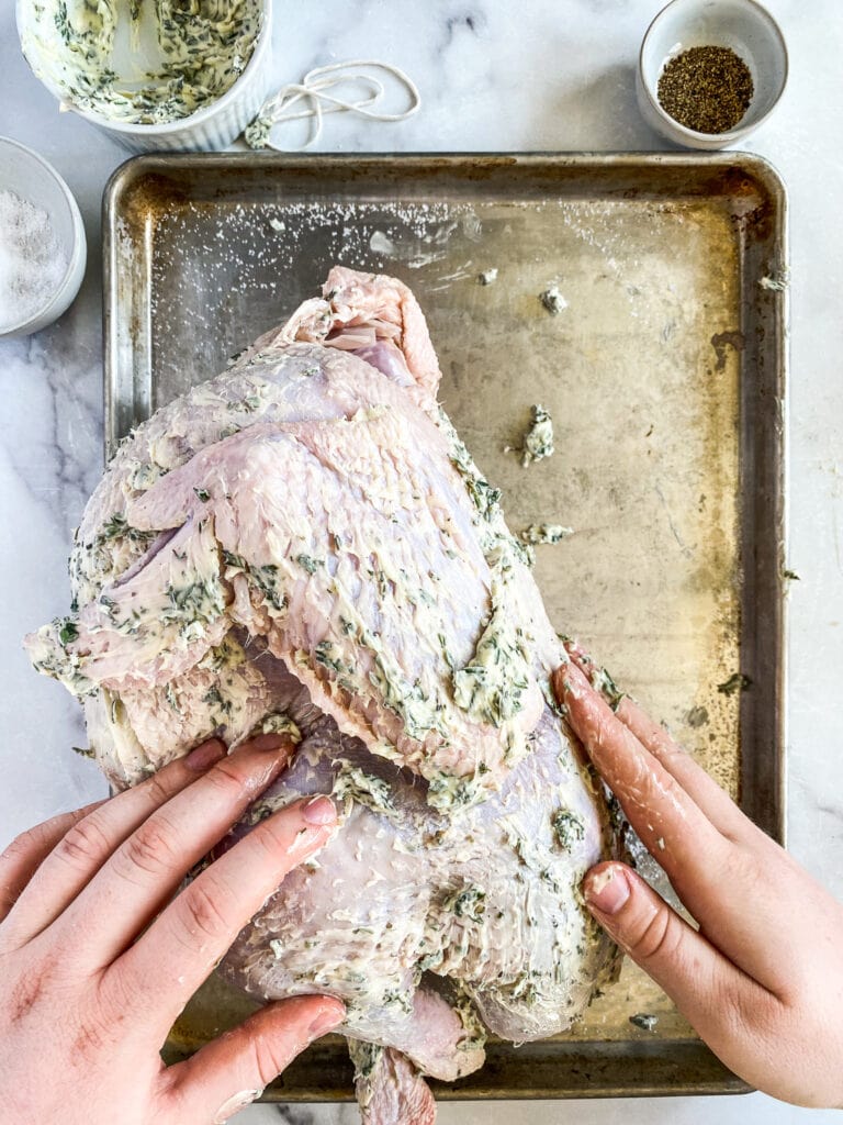 raw bird being slathered with compound butter, inside and out.