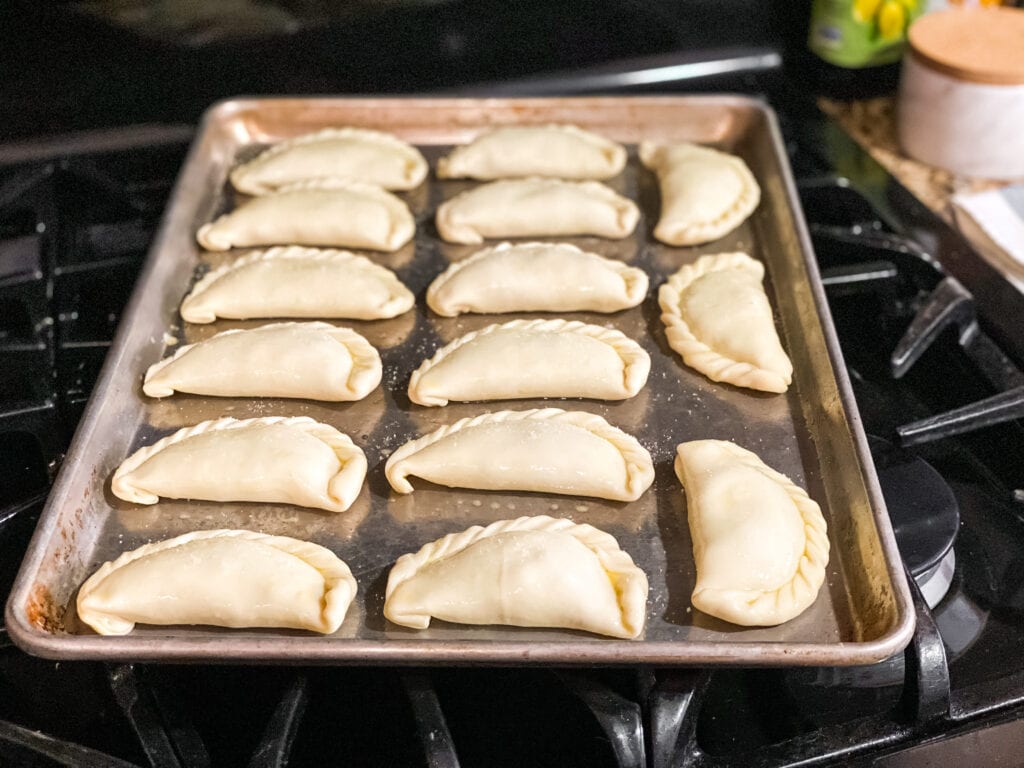 assembled empanadas on a baking sheet ready to go in the oven.