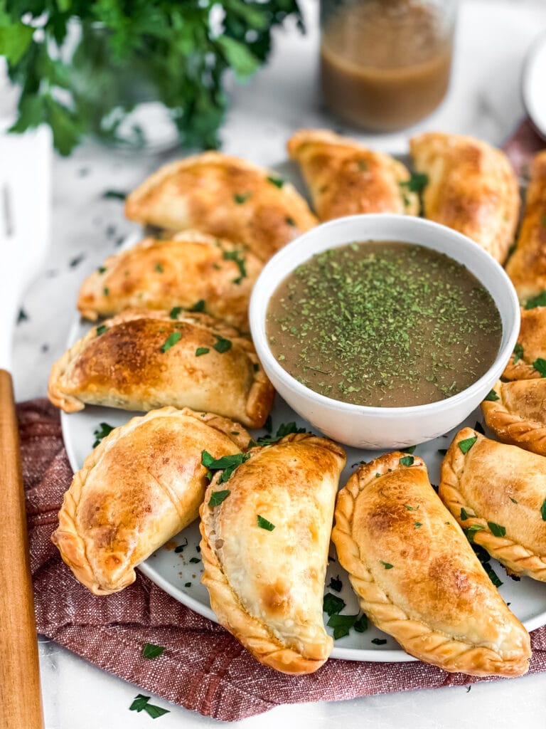 thanksgiving leftover empanadas, cooked and on a serving platter with gravy for dipping. The empanadas are garnished with fresh parsley.