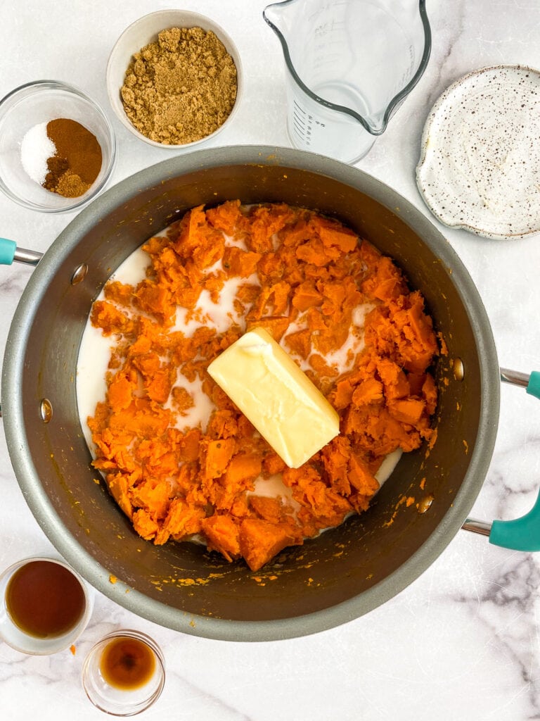 mashed sweet potatoes in a pot with milk poured over and butter on top but not mixed in.