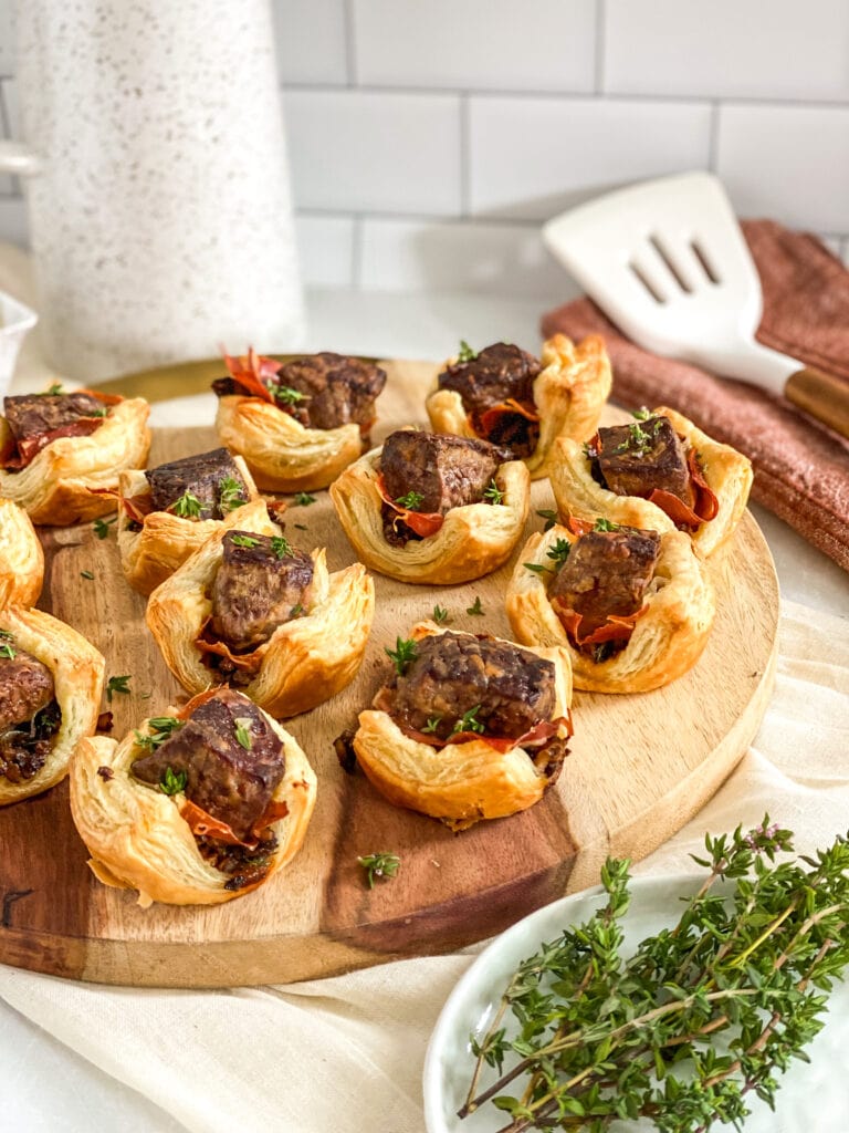 final photo of beef wellington bites on serving tray with dipping sauce in the background and fresh thyme as a garnish.