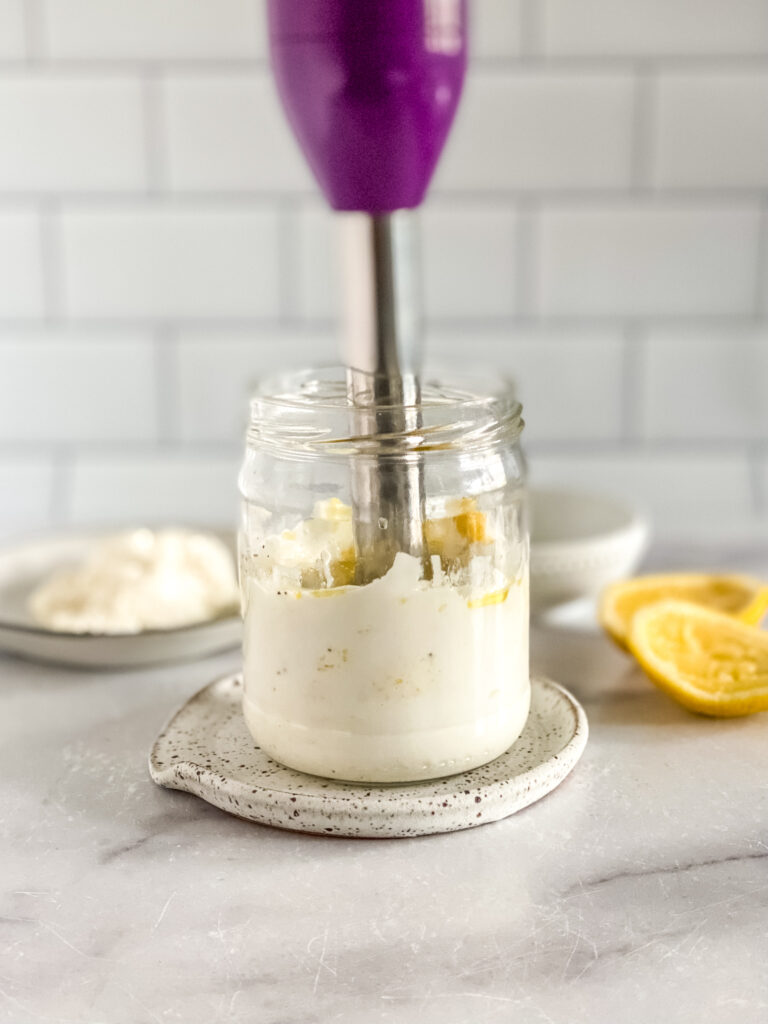 whipped feta ingredients in a glass jar being blended with an immersion blender.