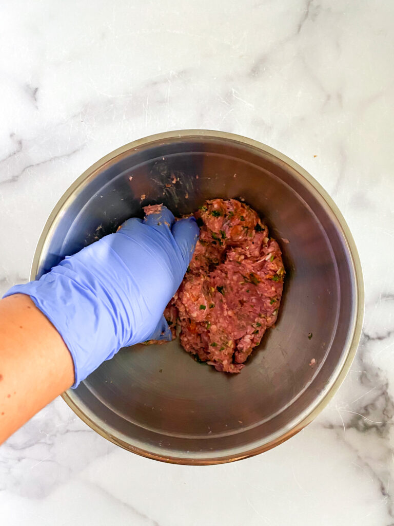 lamb burger mixture being mixed up with a gloved hand.