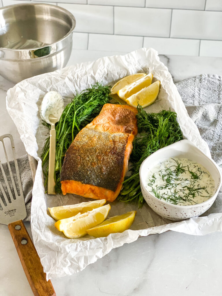 crispy skin salmon with dill sauce on a serving tray with lemons in the background.