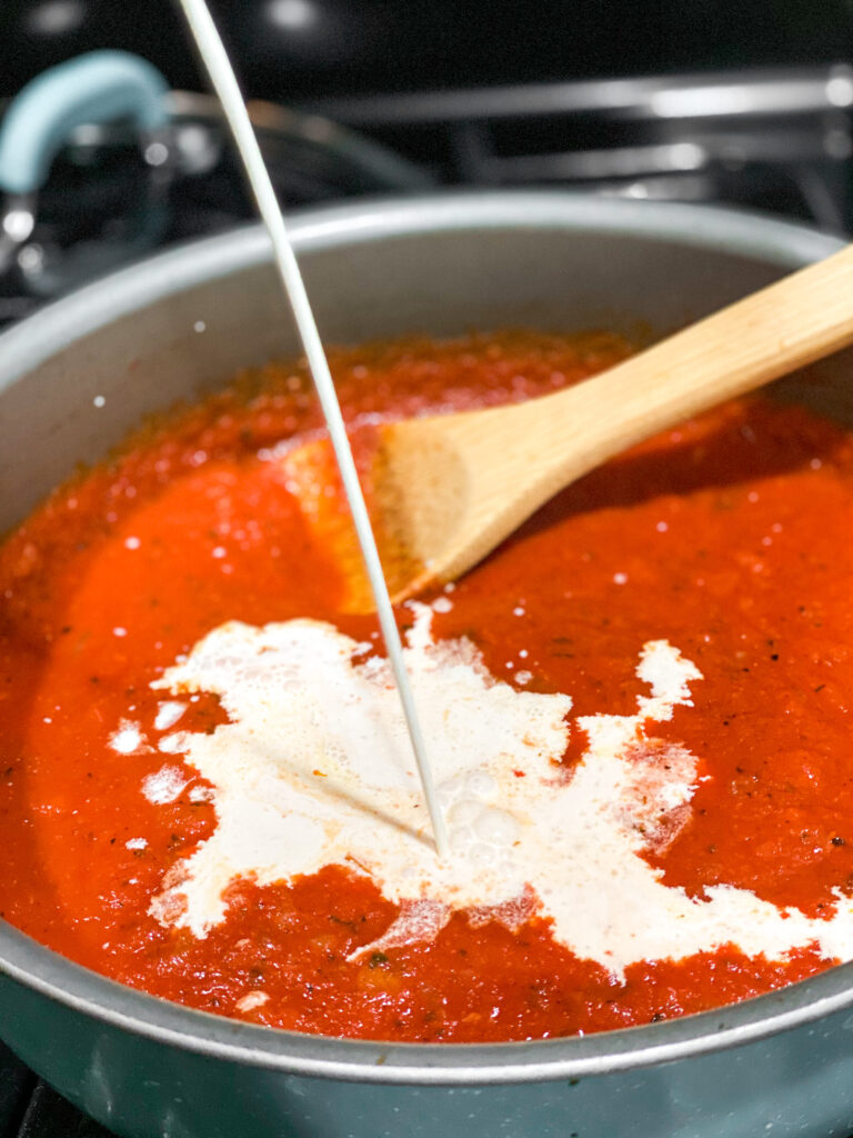 tomato sauce in a sauté pan with cream being added into it.