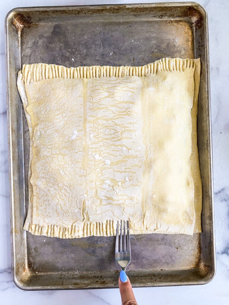 cheesesteak pie with top sheet of puff pastry being sealed around the edges with a fork